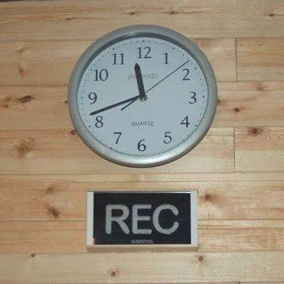 Zwart bordje met REC onder een klok op een houten wand