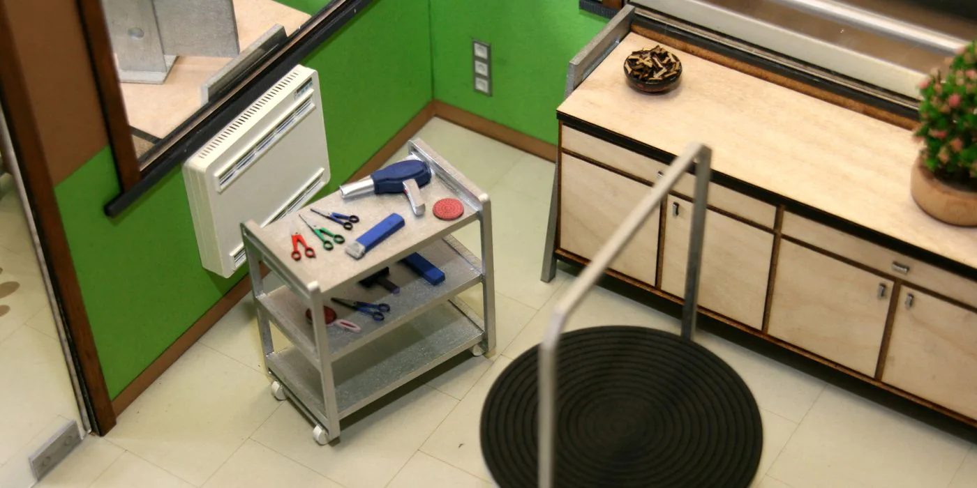 Maquette van een kapsalon met kasten, een rolwagen met schaartjes en een ronde mat